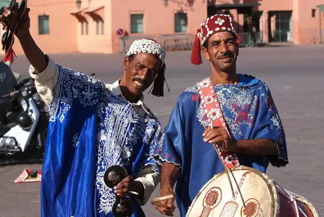 Traditional Moroccan musicians in colorful attire performing in Jemaa el-Fnaa square, creating a lively atmosphere in Marrakech.